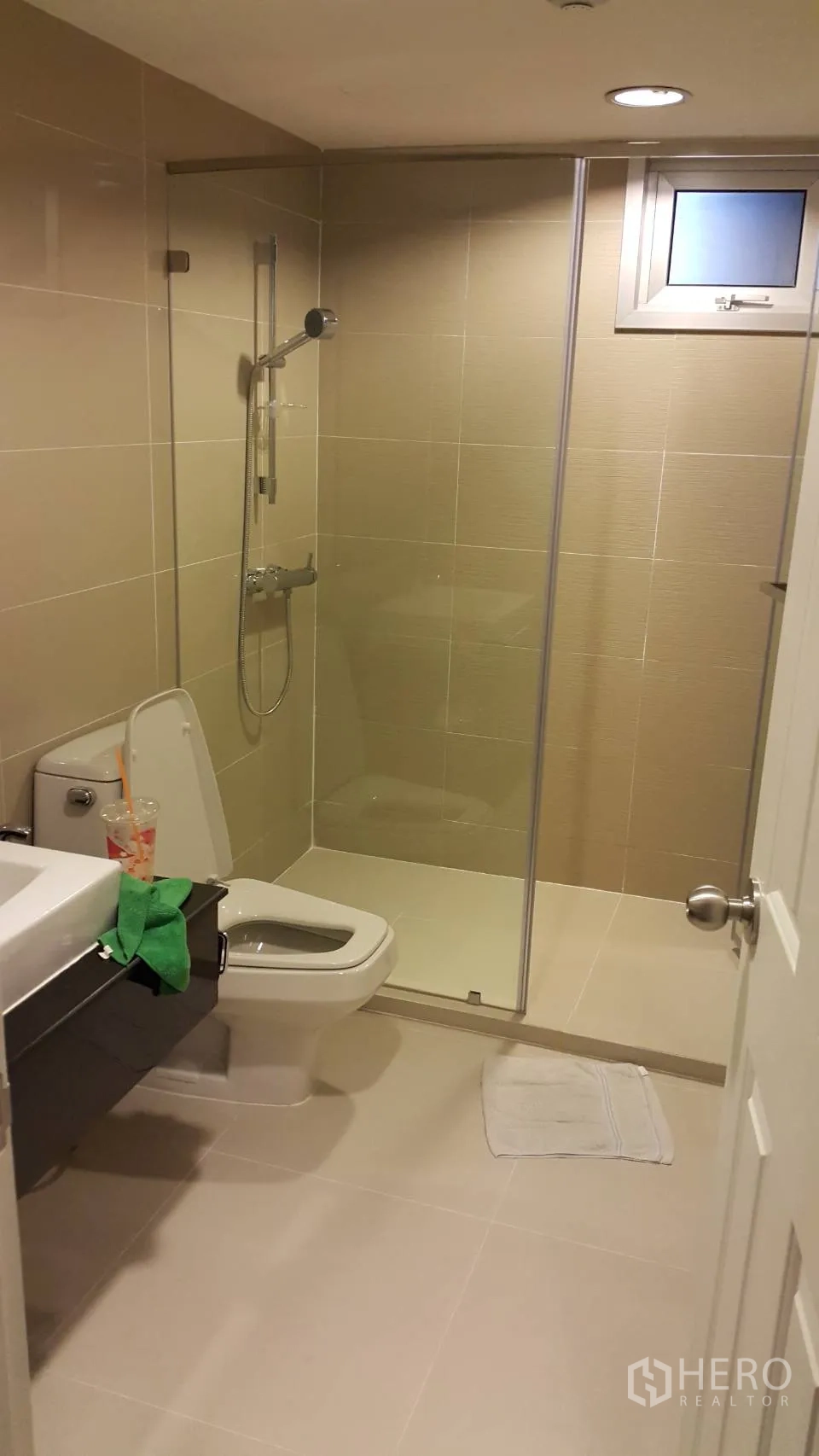 Condominium for rent in Huai Khwang, Bangkok - Contemporary bathroom with glass-enclosed shower, handheld showerhead and beige tiles.