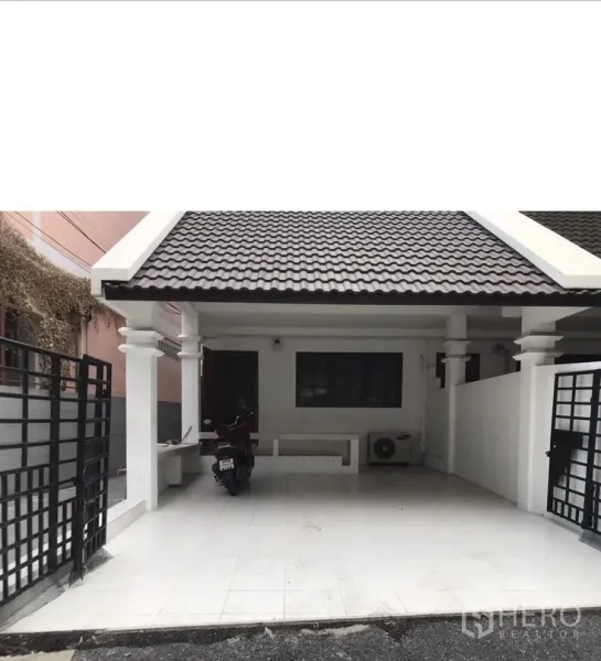 联排别墅 出租在Watthana, Bangkok - 近景车棚，白色立柱、黑色金属门与瓷砖地面