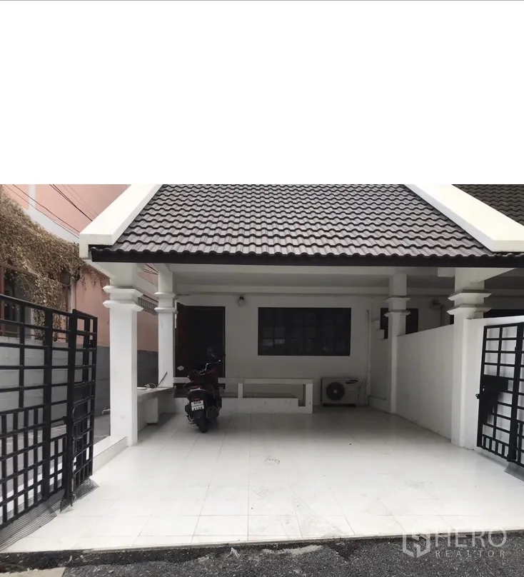 联排别墅 出租在Watthana, Bangkok - 近景车棚，白色立柱、黑色金属门与瓷砖地面