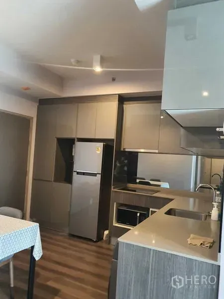 Condominium for rent - Modern L-shaped kitchen with stone countertop, electric hob, oven and full-size fridge over wood-look flooring.