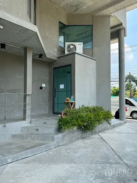 Home Office for rent or sale in Prawet, Bangkok - Main entrance with glass door, steps, and planter, showcasing minimalist concrete design.
