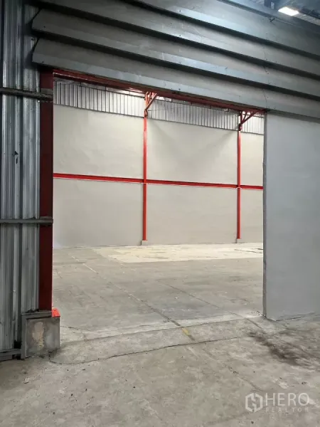 Warehouse for rent in Lat Lum Kaeo, Pathum Thani - View through a large door to an open warehouse bay with red columns and concrete flooring.