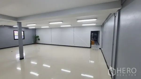 Home Office for rent in Pathum Thani - Spacious open-plan workspace with strip lighting, grey walls and doorway to additional rooms.