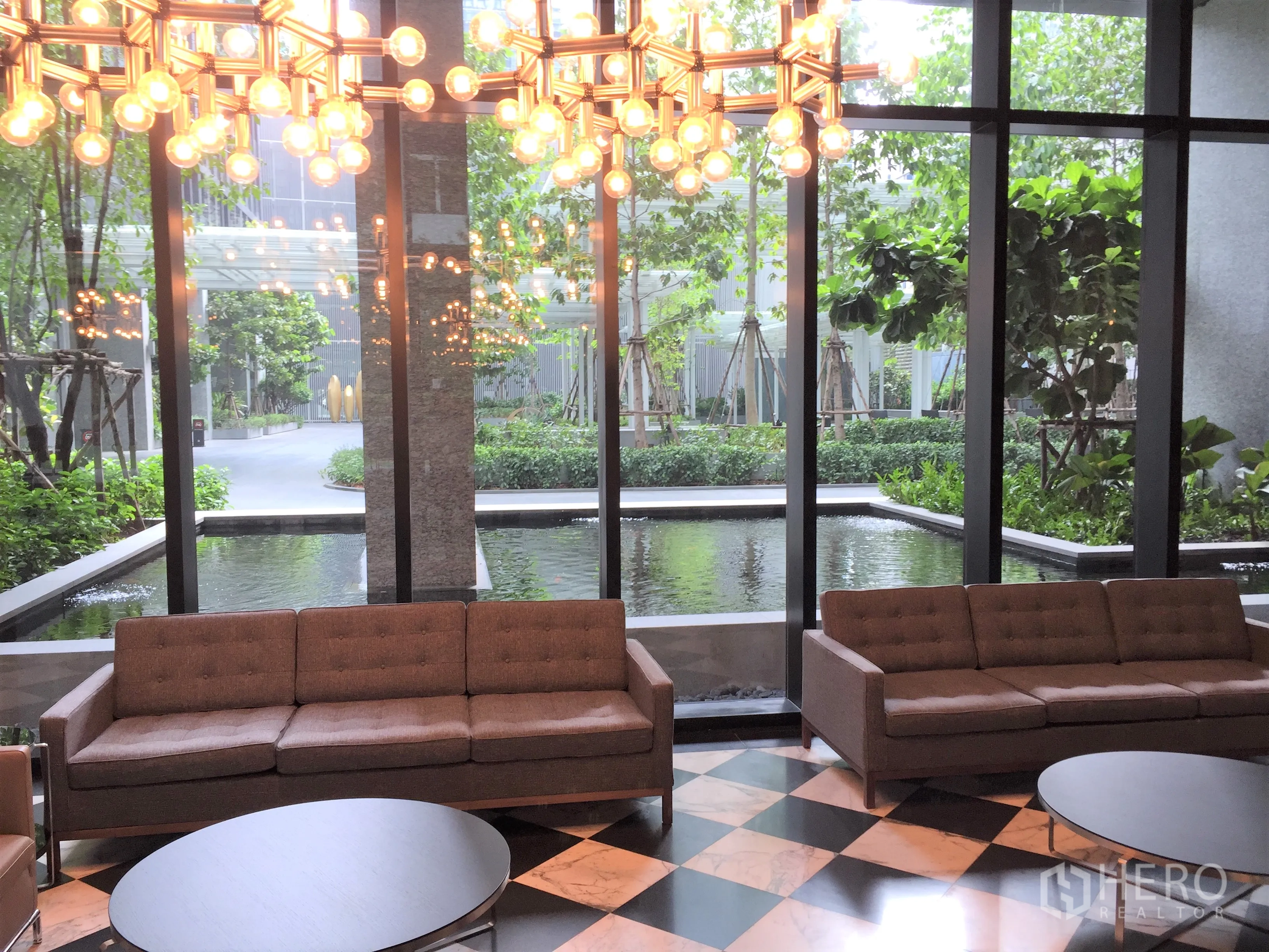 Condominium for rent in Pathum Wan, Bangkok - Elegant condo lobby with sofas, statement chandelier and landscaped pond view.