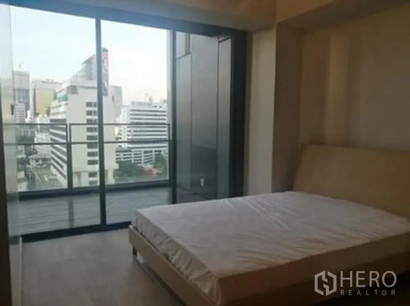 Condominium for sale in Sathon, Bangkok - Bedroom with floor‑to‑ceiling windows opening to a balcony and skyline view.