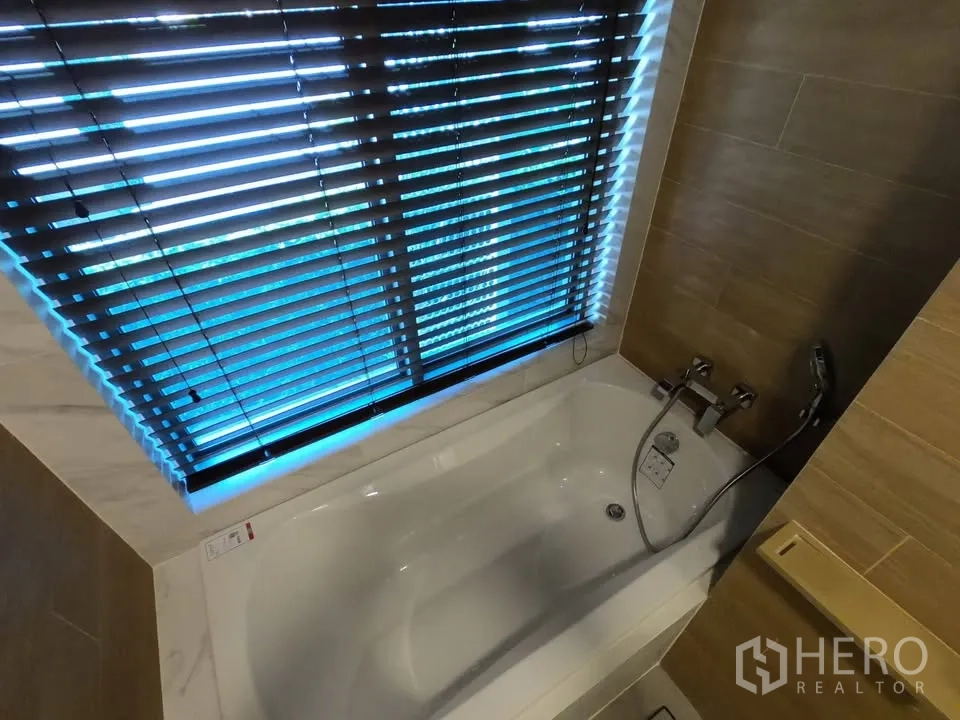Condominium for rent in Watthana, Bangkok - White bathtub under a window with blinds and handheld shower.