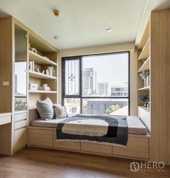 Condominium for rent or sale in Phra Khanong, Bangkok - Multipurpose room with built-in daybed, under-bed drawers and shelving by a picture window with urban view.