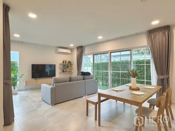 独立式住宅 出租在Bang Phli, Samut Prakan - 宽敞起居区配电视与置物架，环窗俯瞰草坪。