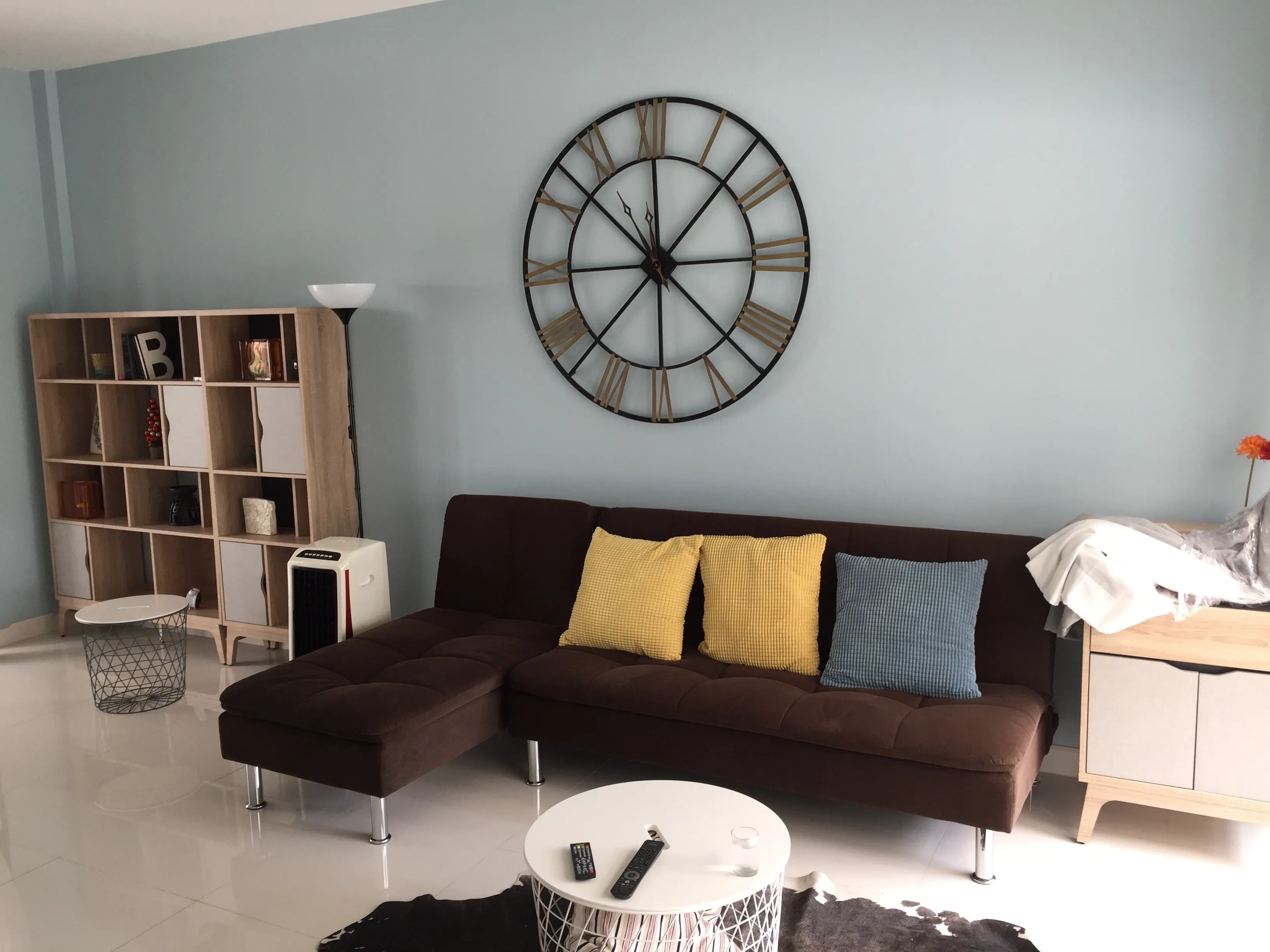 Townhouse for rent in Saphan Sung, Bangkok - Lounge area with brown sectional sofa, colorful cushions, shelving and round coffee tables.