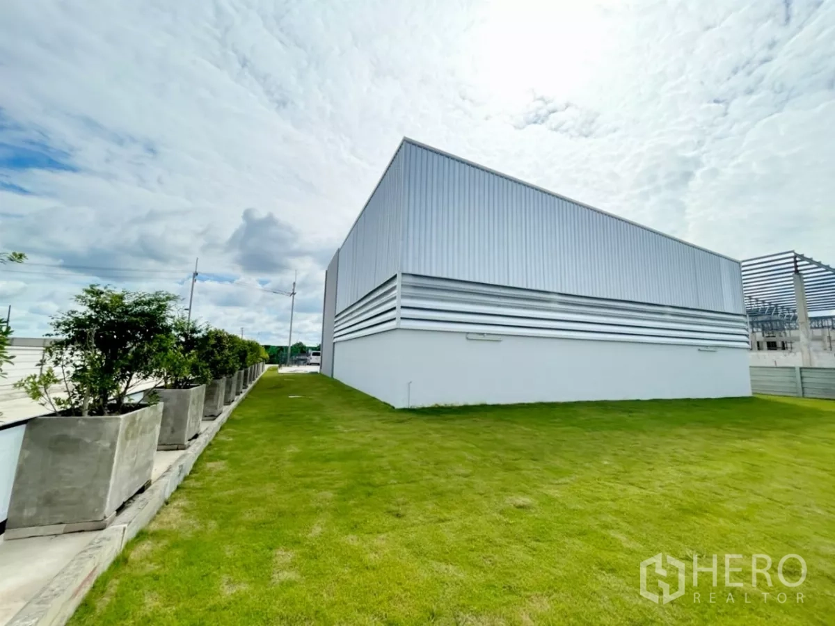 คลังสินค้า ขายในLam Luk Ka, Pathum Thani - สนามหญ้าและกระถางต้นไม้เรียงรายข้างอาคารโกดังผนังเมทัลชีท