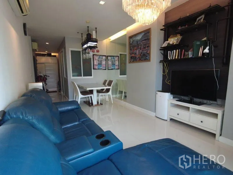 Condominium for rent in Watthana, Bangkok - Open-plan living and dining with blue sofa, TV wall unit and chandelier.
