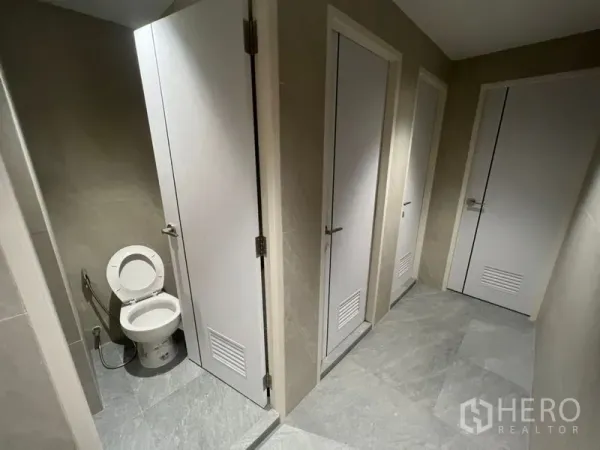 Office Space for rent in Watthana, Bangkok - Corridor of modern restrooms with multiple cubicles and gray stone-look tiles.
