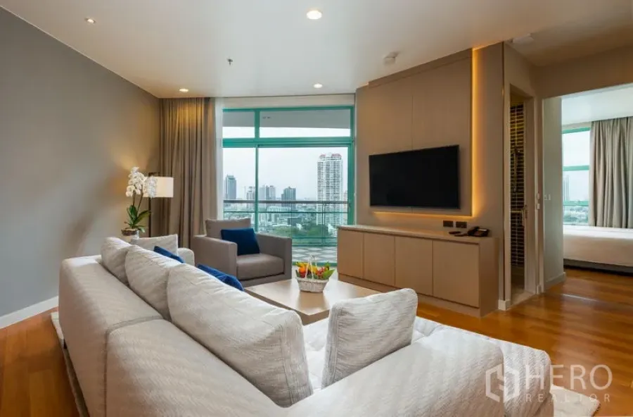Condominium for rent in Bang Kho Laem, Bangkok - Bright living room with sectional sofa, TV console and full-height windows to skyline views.