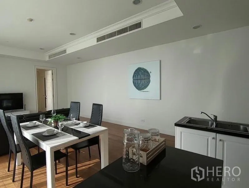 Condominium for rent in Watthana, Bangkok - Four-seat dining area beside a minimalist white pantry and TV in a light-filled room.