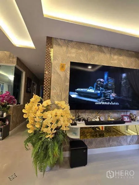 Detached House for rent in Thanyaburi, Pathum Thani - Stylish living area showing TV wall, golden accents and large flower arrangement.