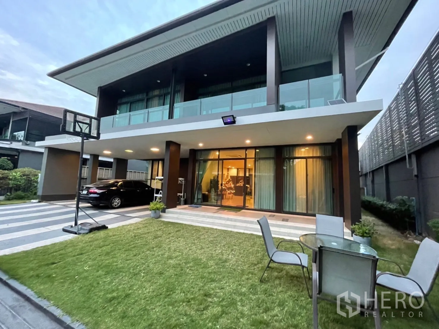 Detached House for rent or sale in Bang Kapi, Bangkok - Modern two-storey detached house with glass balcony, lawn and covered carport at dusk in Bang Kapi.
