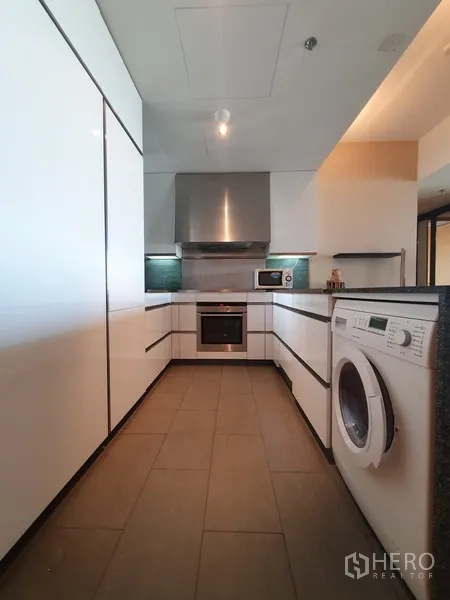Condominium for rent in Sathon, Bangkok - Galley kitchen with white cabinets, oven, range hood and in-unit washing machine.
