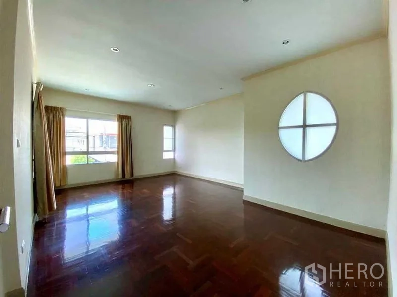 Detached House for sale in Phasi Charoen, Bangkok - Upstairs bedroom featuring polished parquet flooring, a round feature window, and natural light.