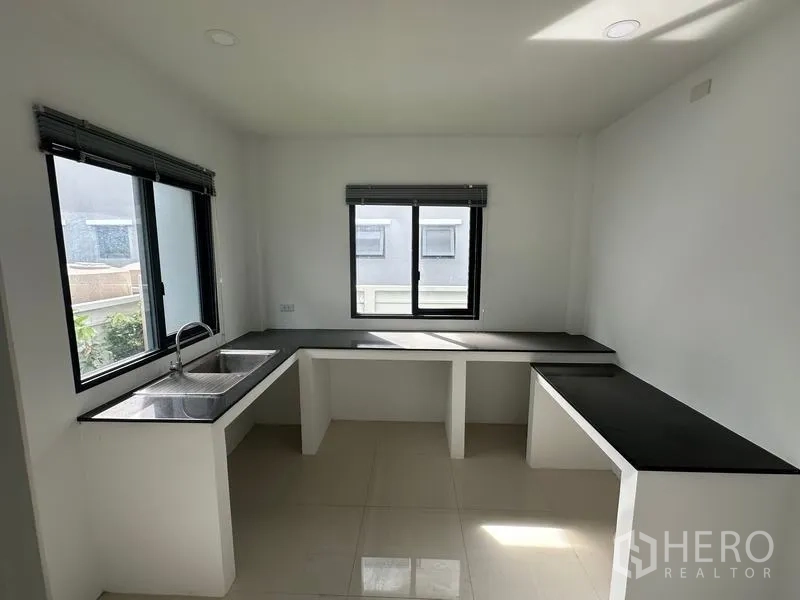 Detached House for sale in Nonthaburi - Bright Thai kitchen with double sink, black countertops and corner windows.