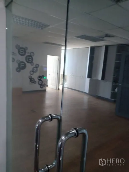 Office Space for rent - Frameless glass double-door entrance reflecting spacious office with ceiling lights and cabinetry.