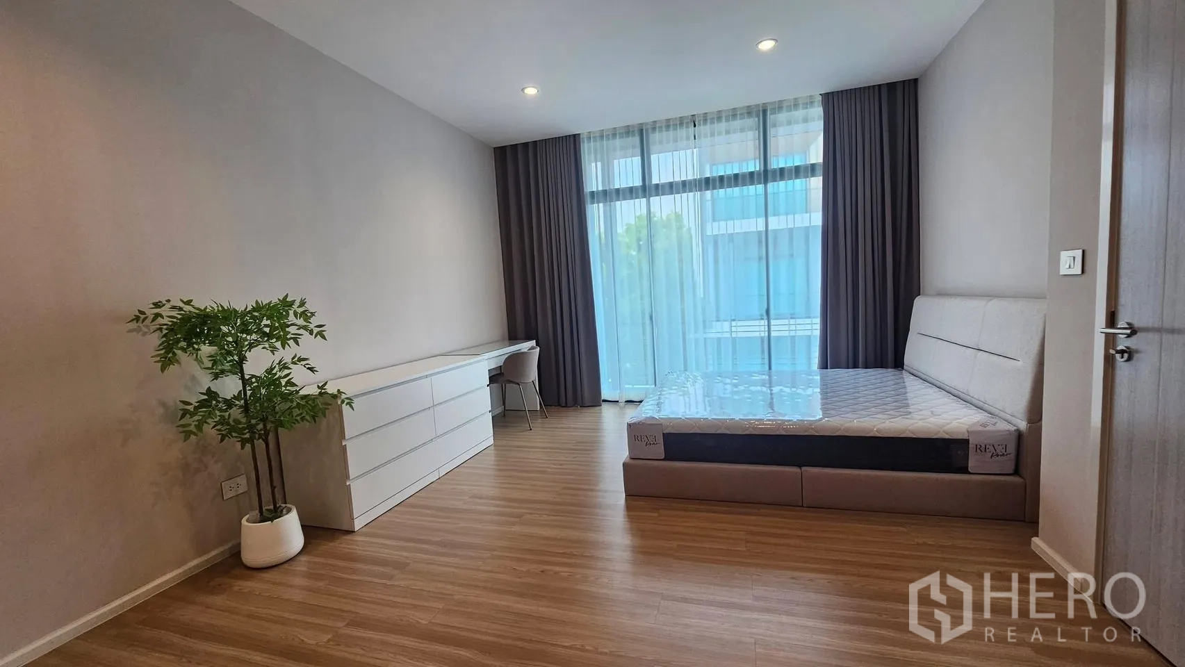 Townhouse for rent in Saphan Sung, Bangkok - Spacious bedroom with upholstered bed, long desk, and large windows with drapes.