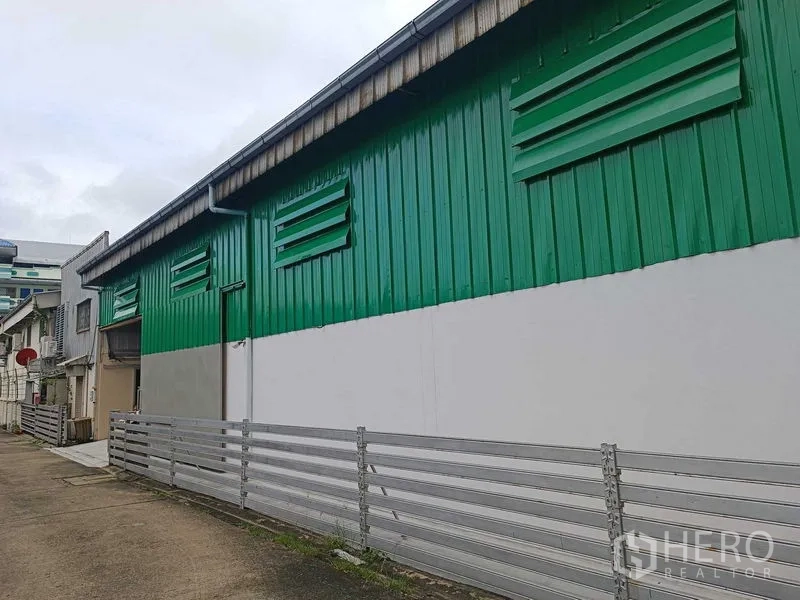 Warehouse for rent in Suan Luang, Bangkok - Alley view of green metal-clad warehouse exterior with louvered vents.