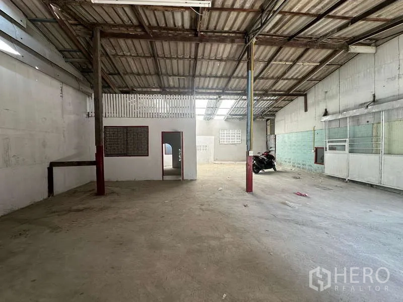 Warehouse for rent in Suan Luang, Bangkok - Secondary warehouse bay with high roof, partitioned rooms, breeze-block windows and a parked scooter.