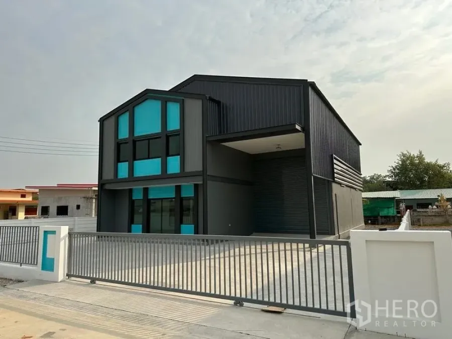 工厂 出租或出售在Bang Bua Thong, Nonthaburi - 工厂外观侧视，带有有顶装卸区、大卷闸门与宽阔水泥车道。