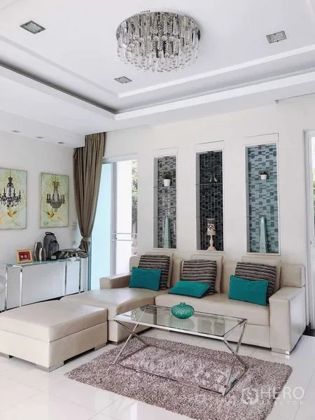 บ้าน ขายในMin Buri, Bangkok - ห้องพักผ่อนพร้อมโซฟาแอล โต๊ะกลางกระจก และผนังตกแต่งช่องนิชใต้โคมคริสตัล