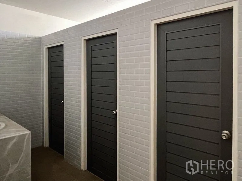 Warehouse for rent or sale - Clean tiled restroom area with three dark grey stall doors and a countertop sink.