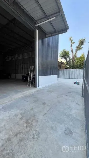 货栈 出租在Bang Khen, Bangkok - 金属外墙仓库的混凝土车道与高挑卷闸入口及雨棚。
