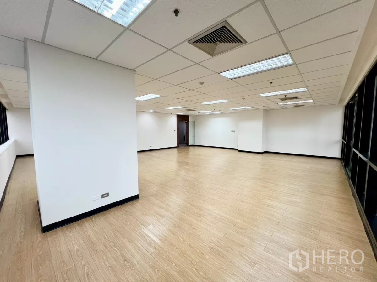 Office Space for rent in Huai Khwang, Bangkok - Open-plan office with wood flooring, perimeter windows, drop ceiling with fluorescent lights and a glass entry door.
