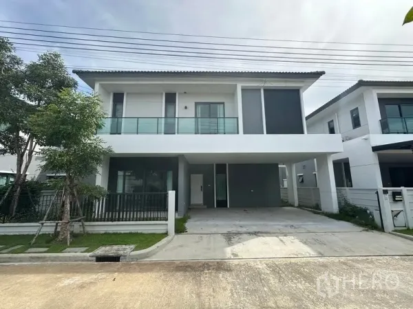 Detached House for sale in Nonthaburi - Modern two-storey detached house exterior with glass balcony and wide driveway under a covered carport.