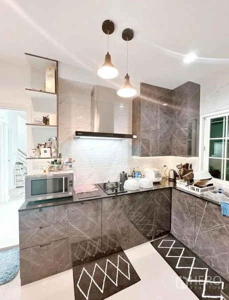 Detached House for rent in Bueng Kum, Bangkok - Modern L-shaped kitchen with stone-look cabinets, gas hob, range hood, microwave and pendant lights.