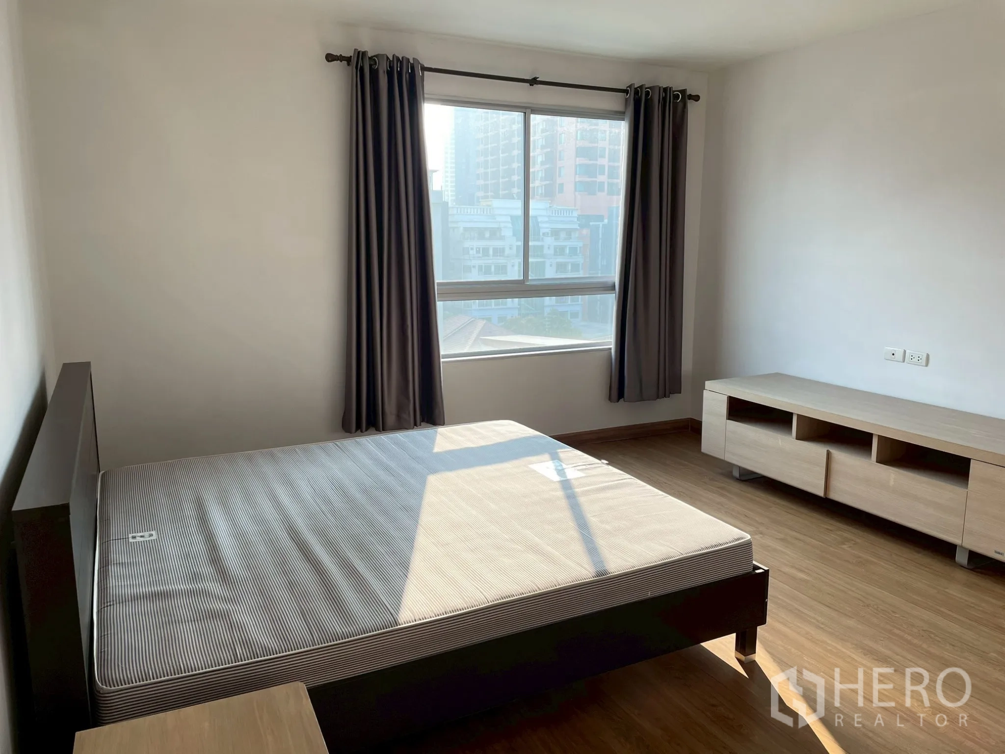 Apartment for rent in Khlong Toei, Bangkok - Sunlit bedroom with double bed frame, large window, and TV console.