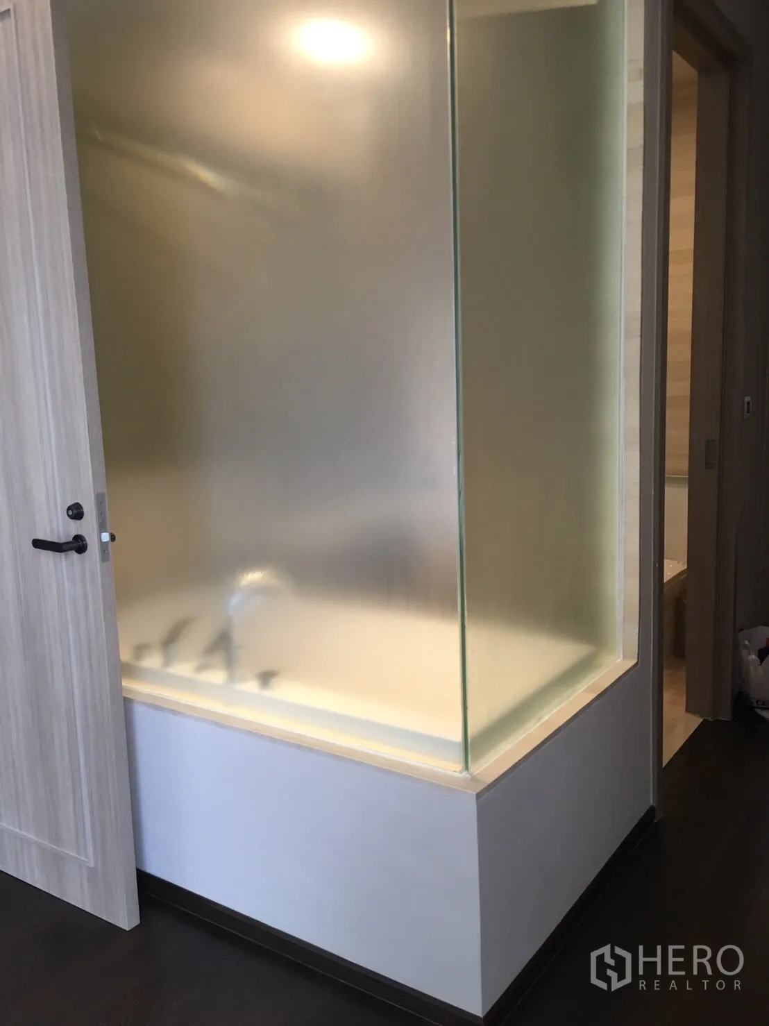 Condominium for rent in Watthana, Bangkok - Close-up of bathroom featuring frosted-glass enclosure around a bathtub and a light wood door.