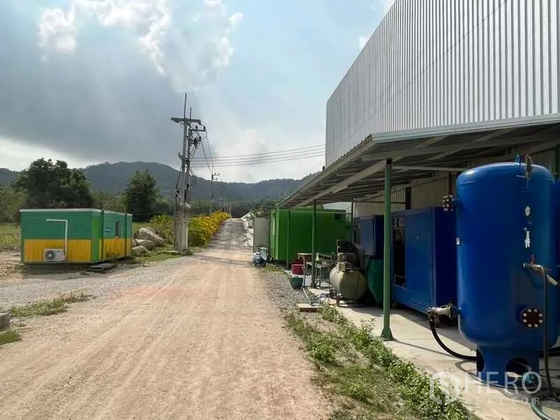 工厂 出售在Nikhom Phatthana, Rayong - 厂房侧道与压力罐设备，远景为乡野与山景。