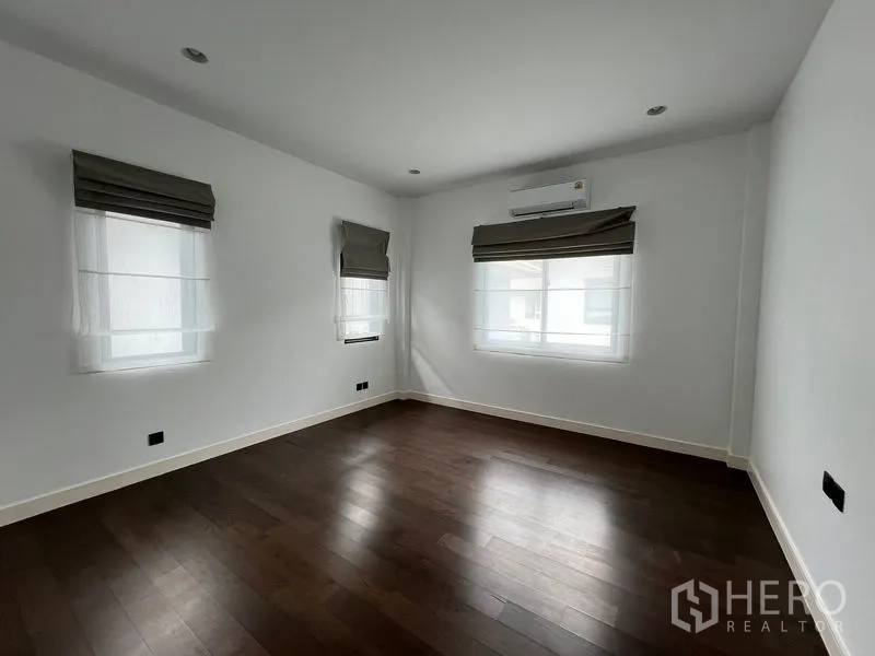 Detached House for rent in Bang Kapi, Bangkok - Bedroom with two windows, wall-mounted air conditioner and wood floors.