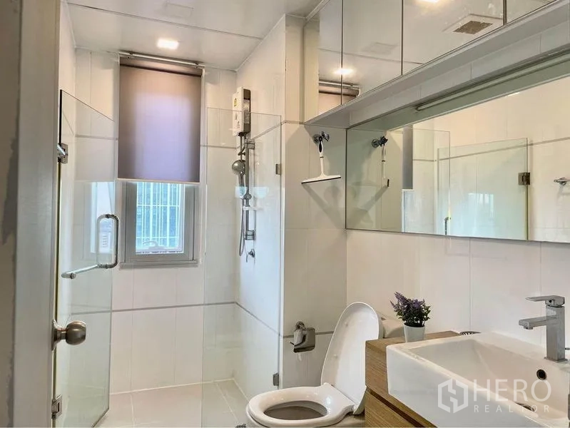 Condominium for rent in Huai Khwang, Bangkok - Bright bathroom with glass-enclosed shower, vanity and mirrored cabinets.