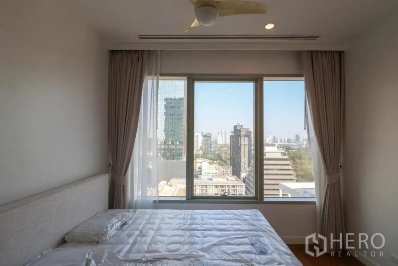 Condominium for rent in Pathum Wan, Bangkok - Bedroom with wide window, curtains and downtown city view.