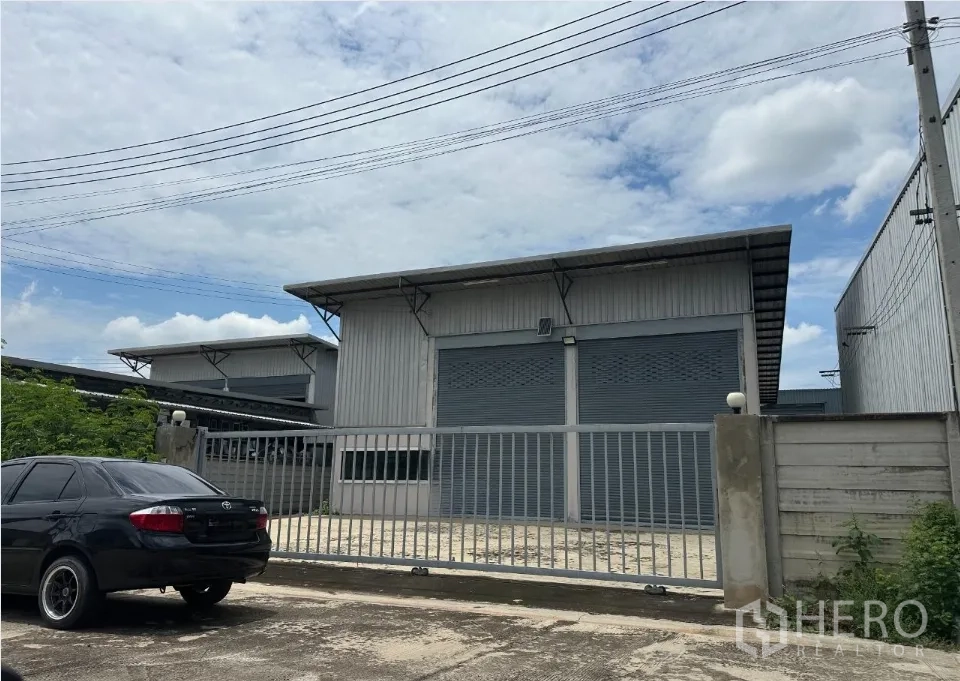 Warehouse for sale in Bang Len, Nakhon Pathom - Gated industrial warehouse with grey exterior, twin roller shutters and parking apron in front.