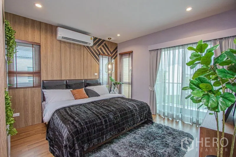 Detached House for sale in Lam Luk Ka, Pathum Thani - Primary bedroom with wood-panel accent wall, king bed, air conditioning and floor-to-ceiling curtains.