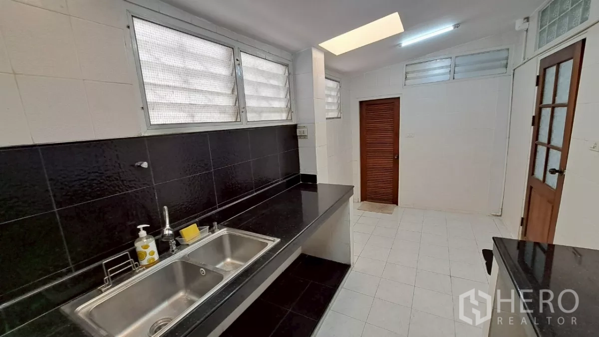 Townhouse for rent in Watthana, Bangkok - Bright kitchen with black countertops, double sink and louvered windows.