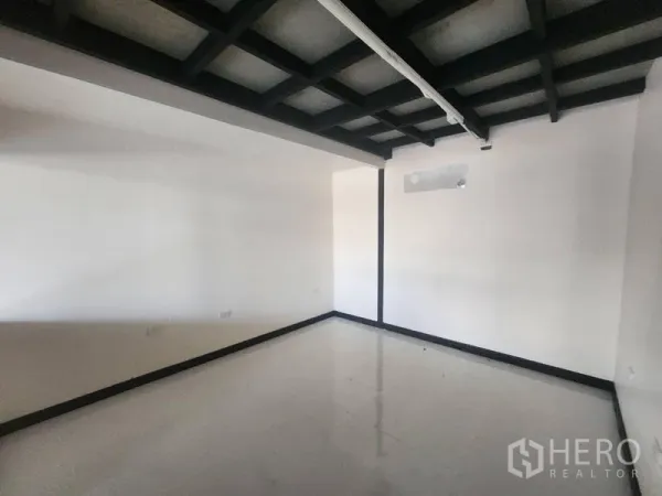 Warehouse for rent in Suan Luang, Bangkok - Empty ground-floor room with white walls, black grid ceiling and glossy tile flooring.