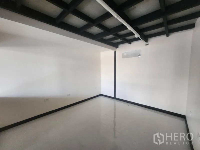 Warehouse for rent in Suan Luang, Bangkok - Empty ground-floor room with white walls, black grid ceiling and glossy tile flooring.