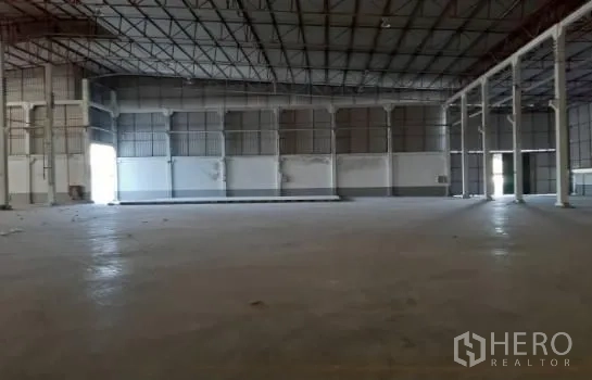 Warehouse for rent in Mueang Samut Sakhon, Samut Sakhon - Open storage hall with steel roof structure, grid columns and roller shutter doors.