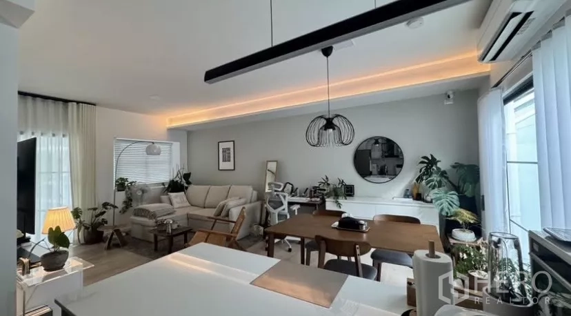 Townhouse for rent in Bang Phli, Samut Prakan - Spacious living and dining area with cove lighting, sofa set, large windows and lush indoor plants.
