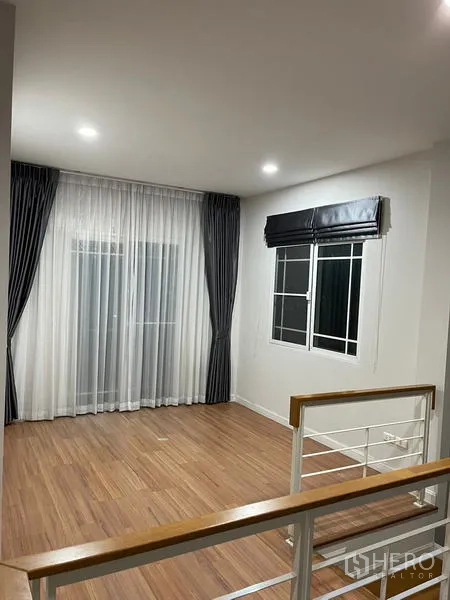 Detached House for rent in Bang Kapi, Bangkok - Upstairs landing with wood flooring, white railing and wide windows with curtains.