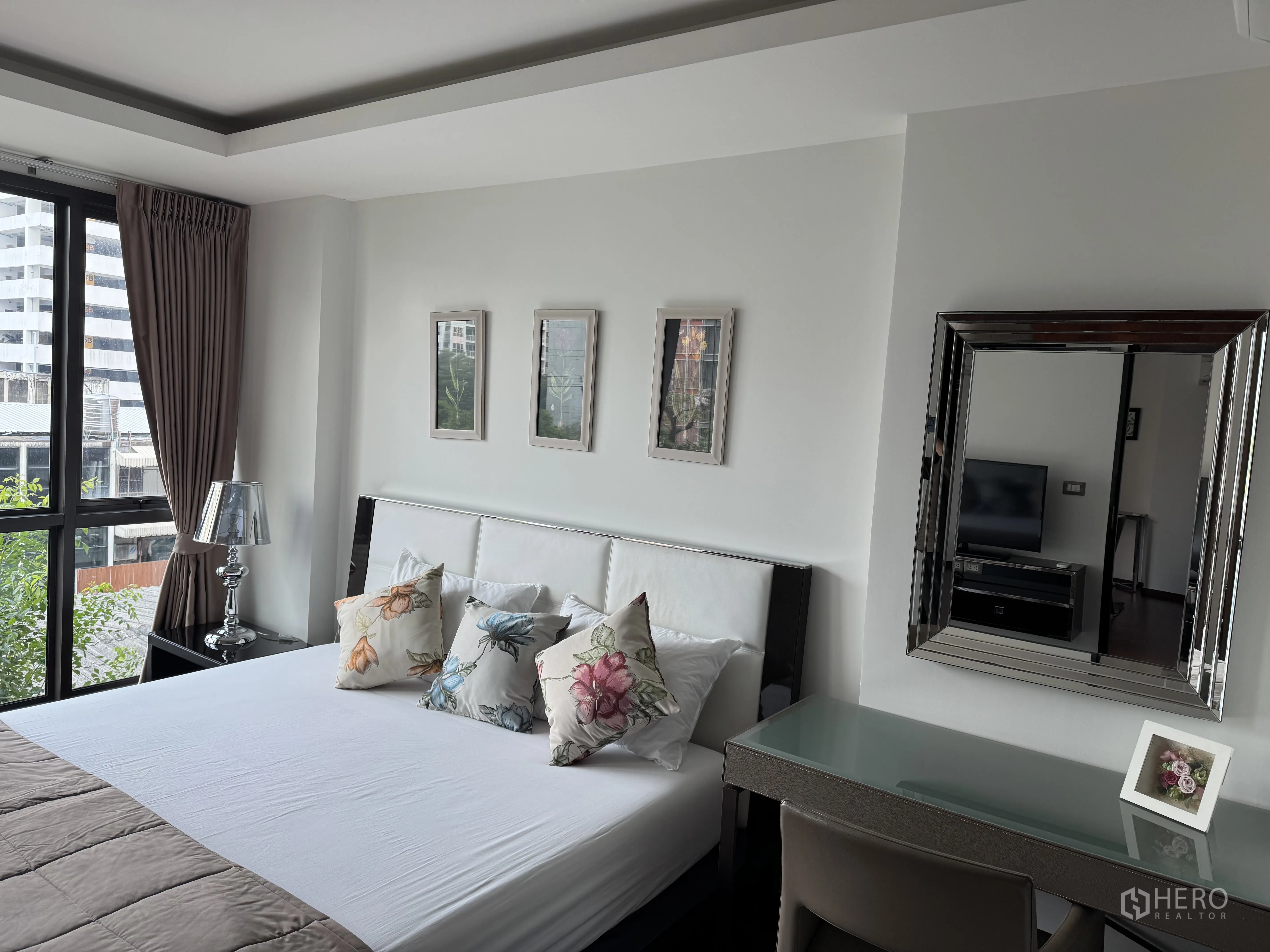 Condominium for rent in Watthana, Bangkok - Second bedroom with corner windows, bed, desk, and decorative mirror.