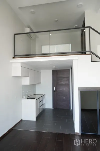 Condominium for sale in Watthana, Bangkok - Open-plan loft with kitchen below and a glass-railed mezzanine above.